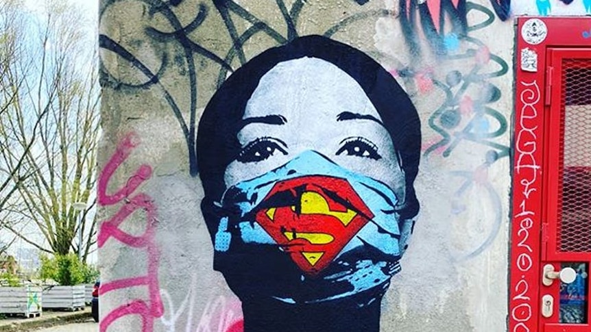 A photo shows a mural of a woman with a superman inspired mask covering her mouth and nose