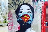 A photo shows a mural of a woman with a superman inspired mask covering her mouth and nose