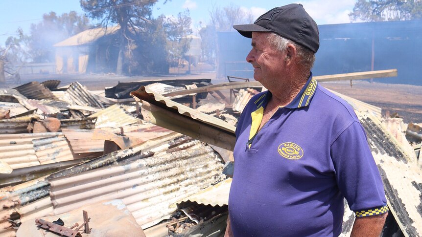A man looks over flattened sheds that are still smouldering from the bushfire.