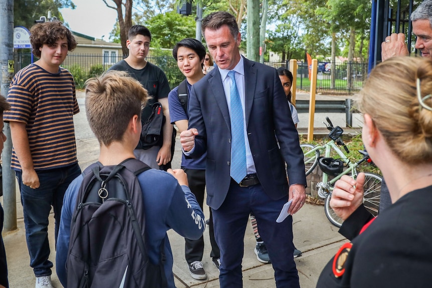 a man standing outdoors surrounded by young people doing a fist bump