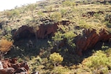 Picture of a cave system in rough Pilbara landscape with few trees and much spinifex above the caves