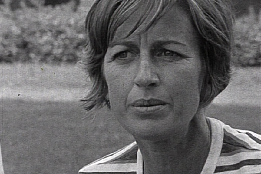 Grainy black and white close up of a woman with fair short hair in a striped short sleeve top. She is outside.