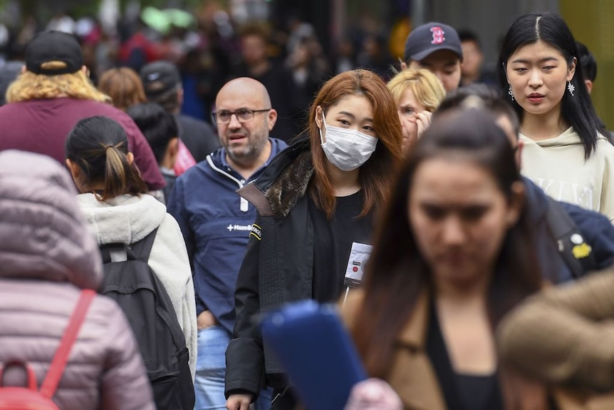 A woman wearing a face mask crosses the street in Melbourne.