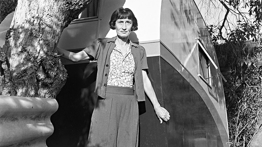 Slim older woman with page boy haircut in front of a 1940s caravan