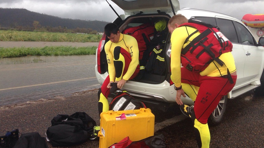 Two men dressing in wet suits, life vests and flippers out the back of a car.