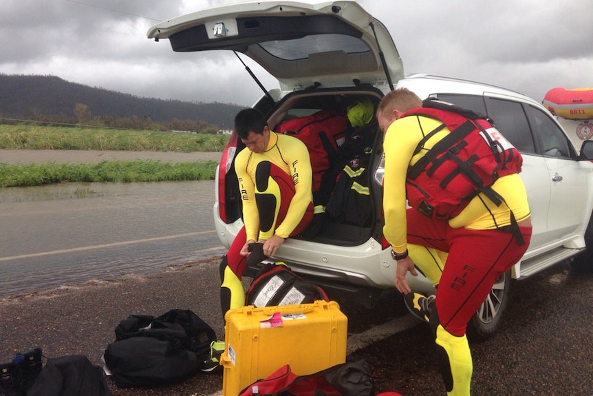 Two men dressing in wet suits, life vests and flippers out the back of a car.