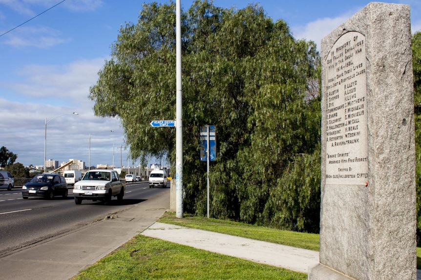 A large stone engraved with names stands next to a busy road