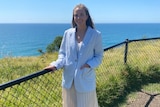 a woman standing next to a fence near a cliff next to the ocean