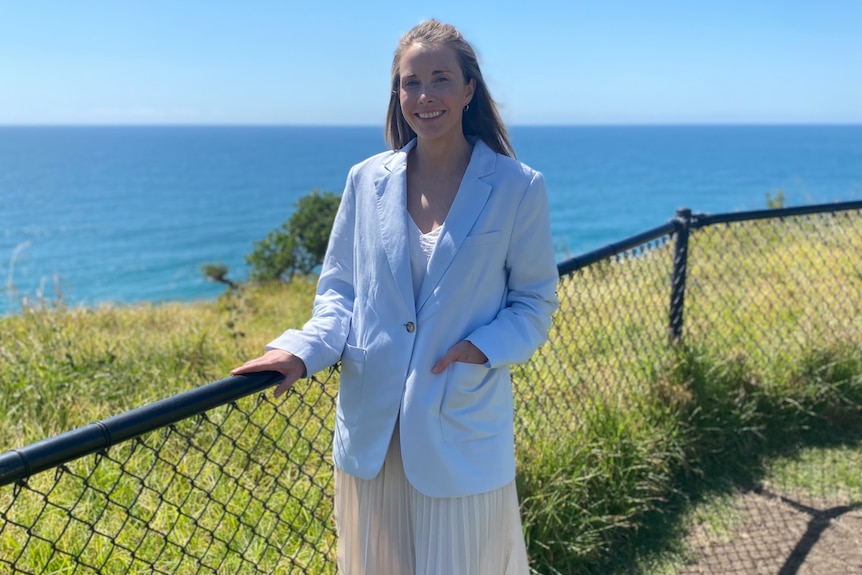 a woman standing next to a fence near a cliff next to the ocean