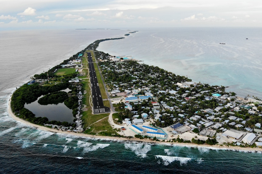 Aerial view of one of Tuvalu's islands: a tear-shaped island with houses very close to the land's edge, surrounded by ocean.