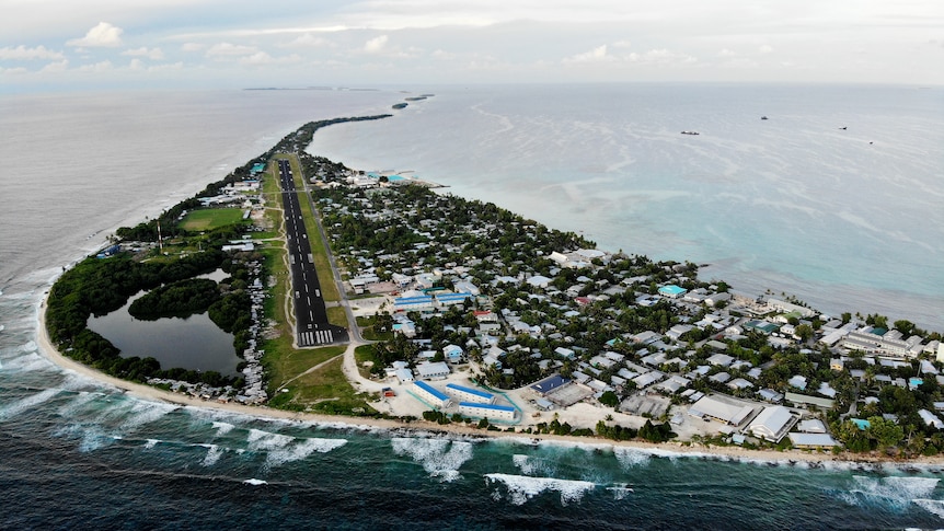 Aerial view of one of Tuvalu's islands: a tear-shaped island with houses very close to the land's edge, surrounded by ocean.