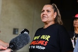 A mid-shot of Raelene Cooper speaking to reporters outside court in Perth, wearing a shirt reading 'save our songlines'.