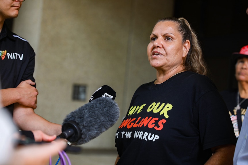 A mid-shot of Raelene Cooper speaking to reporters outside court in Perth, wearing a shirt reading 'save our songlines'.