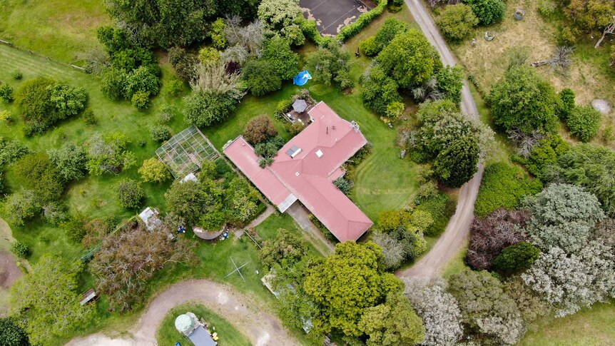 A drone shot shows many large green trees, a greenhouse, tennis court and farm appliances surrounding the Bokensha home.