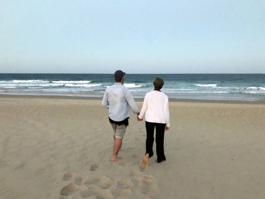 A couple walking toward the beach, holding hands