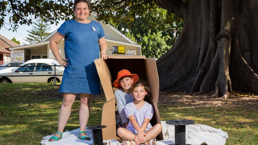 Katie Cadman stands next to a box with kids sitting in it.