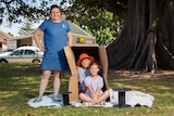 Katie Cadman stands next to a box with kids sitting in it.