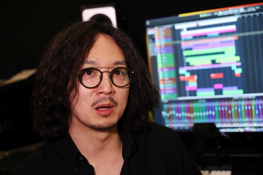 Man in glasses sits in front of music production technology 