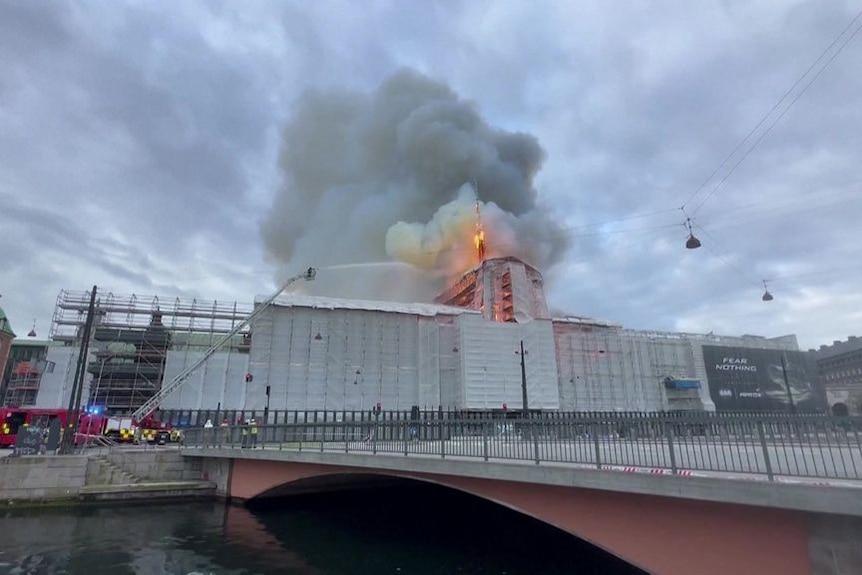 A building with scaffolding around it alight with smoke plumes rising in the air above it.