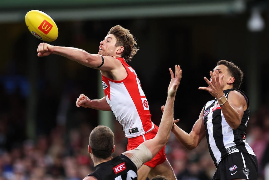 A Sydney Swans defender launches his fist at the ball to punch it clear of Collingwood forwards during a game.