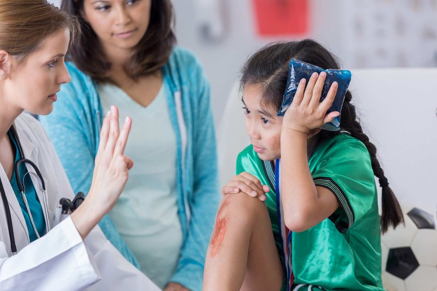 A young girl injured while playing sport is talking to a doctor with her mother in the background