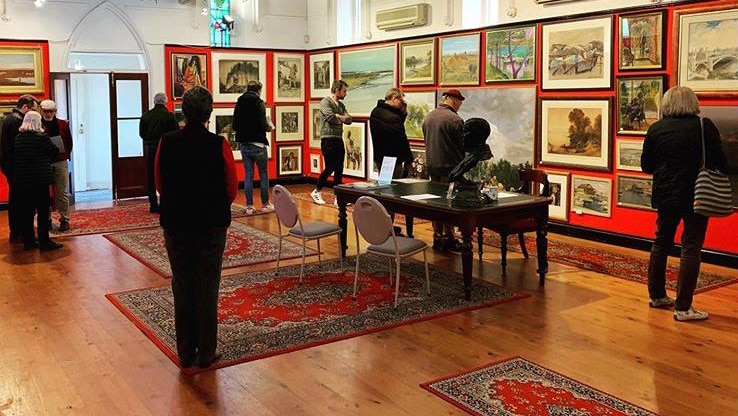 A group of people stand about looking at artwork on walls.