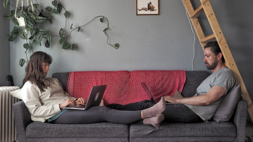 Alex McClintock and his partner sit at opposite ends of a couch, working on their laptops