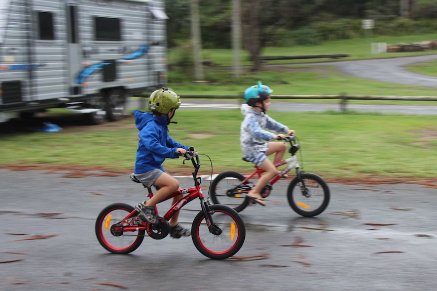 Two boys riding bikes in a caravan park.