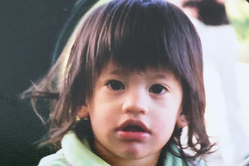 A baby with dark hair smiles at the camera.