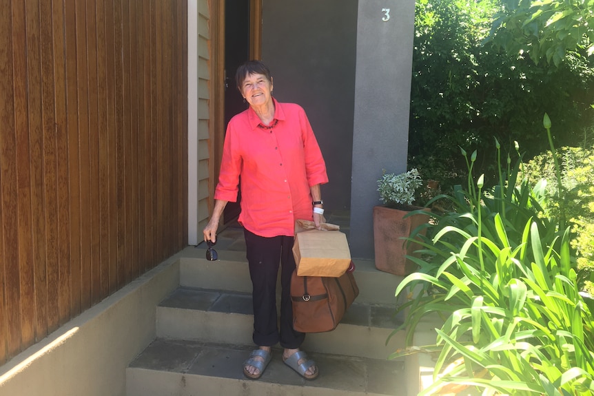 A woman in a pink shirt holding a bag. 