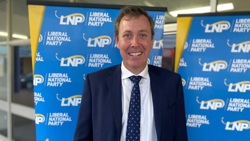 A man in a suit stands in front of an LNP banner.