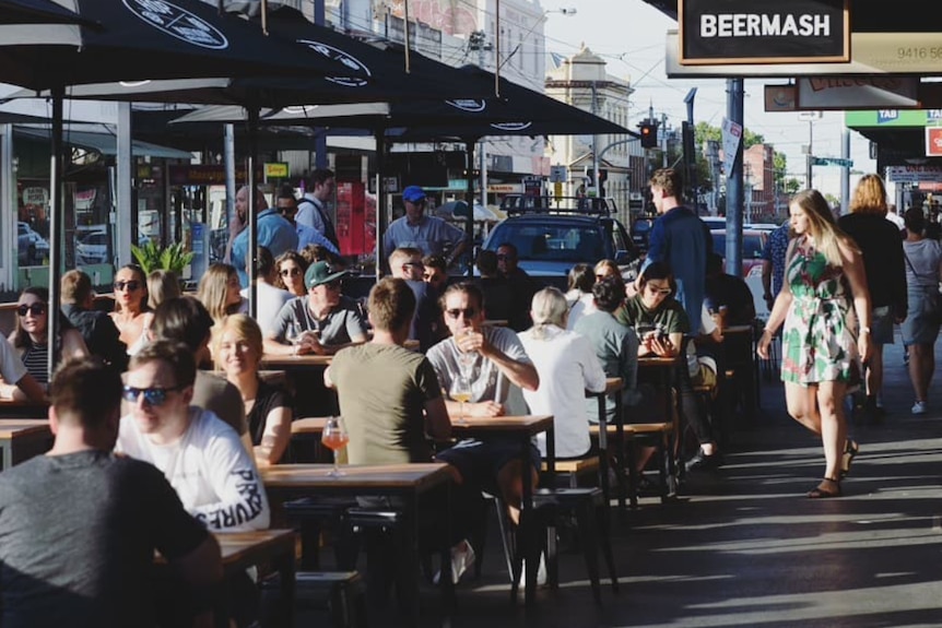 Photo of dozens of people sitting out the front of a busy bar