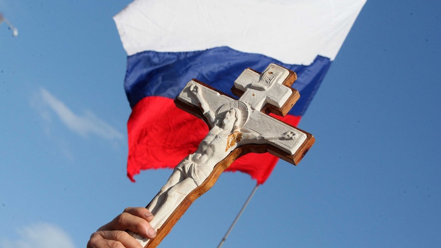 A pro-Russian supporter holds high a crucifix in front of a Russian flag,