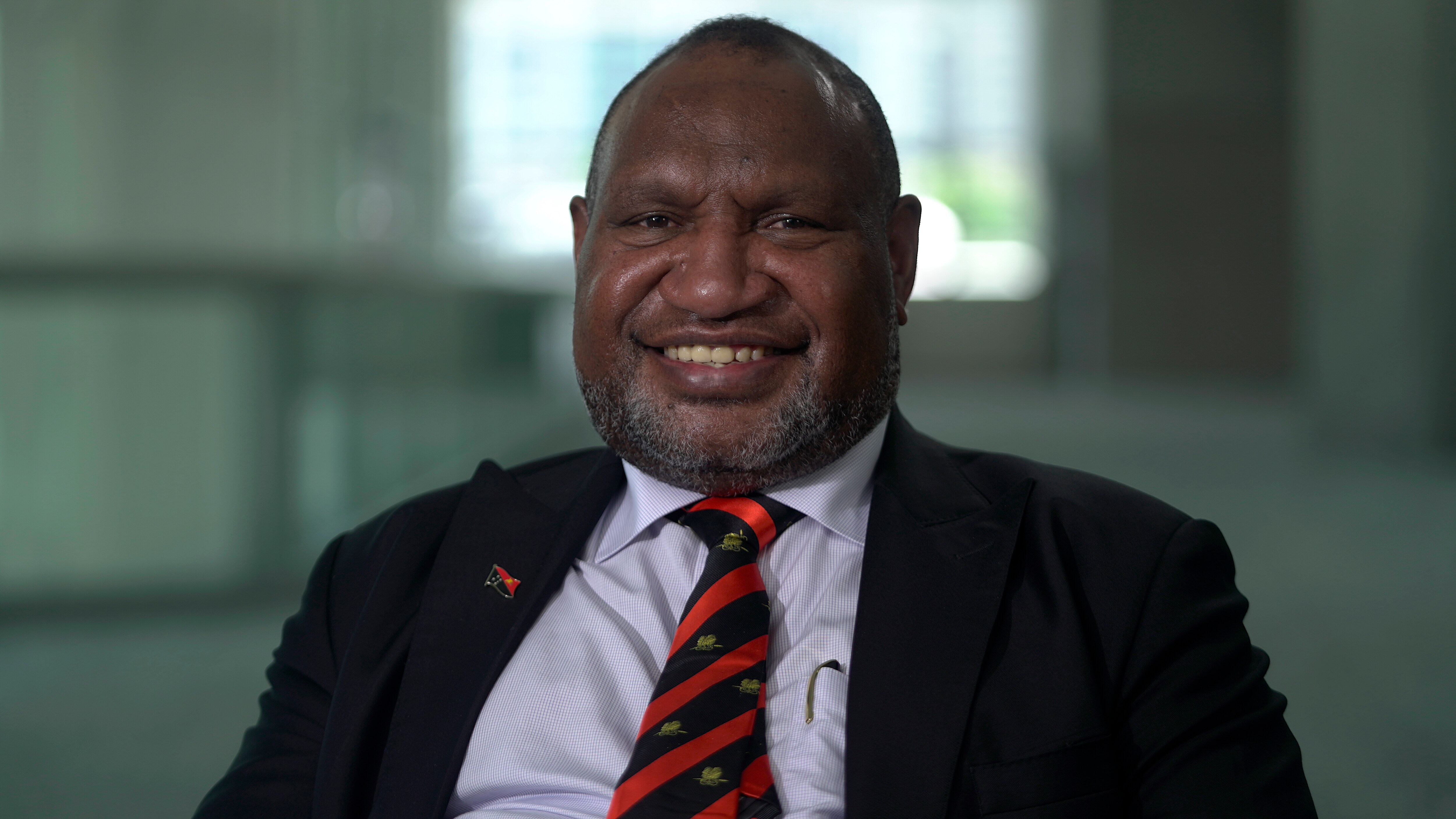 James Marape wearing a black suit and a blue shirt with a black and red tie.