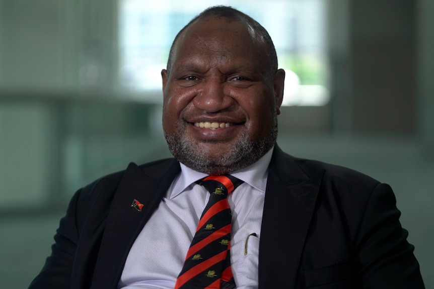 James Marape wearing a black suit and a blue shirt with a black and red tie.