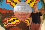 a young girl stands next to a mural.
