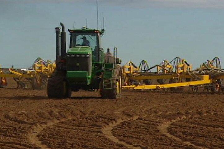 TV still of generic shot of tractor pulling plough equipment across dirt field in Qld.