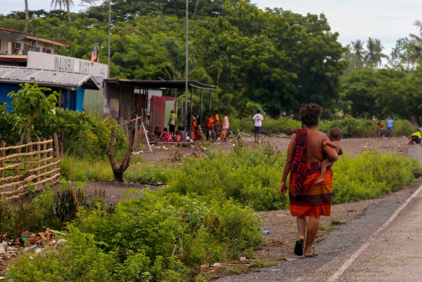 A woman in PNG walking down a road clutching a baby