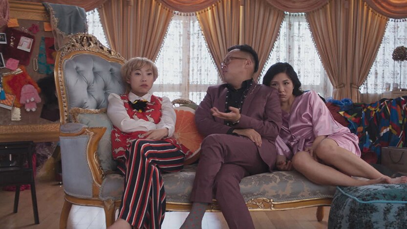 Colour mid-shot still of rapper and actor Awkwafina in a scene with Nico Santos and Constance Wu in 2018 film Crazy Rich Asians.