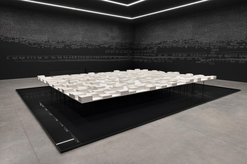 A large table covered with reams of documents sits above black reflective flooring in a room with black walls covered in chalk.