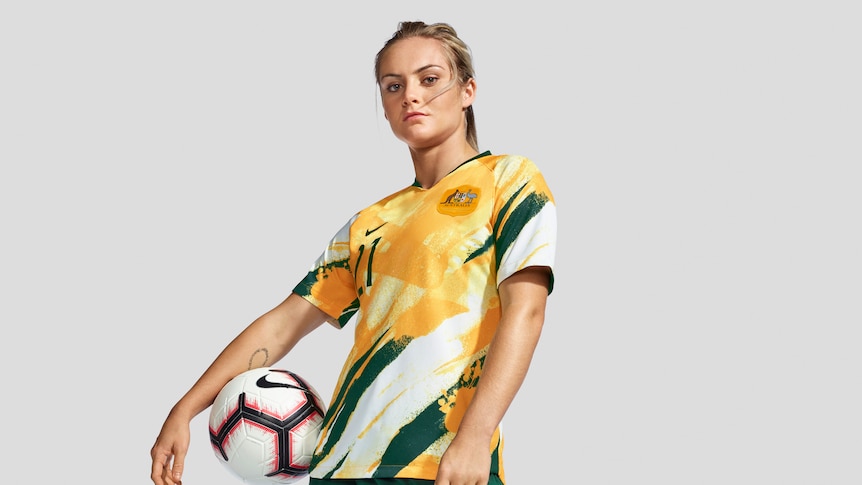 Ellie Carpenter models the new Matildas World Cup kit, yellow shirt, green shorts, white socks.