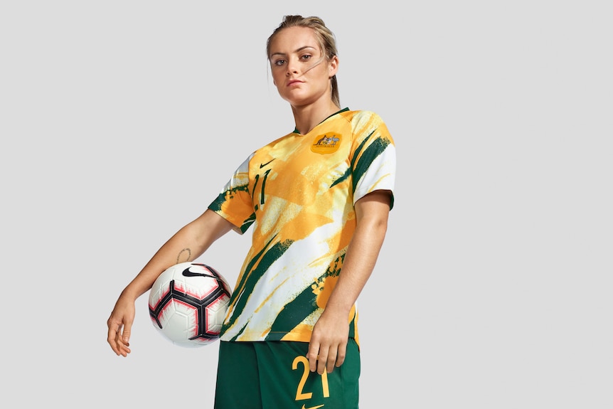 Ellie Carpenter models the new Matildas World Cup kit, yellow shirt, green shorts, white socks.