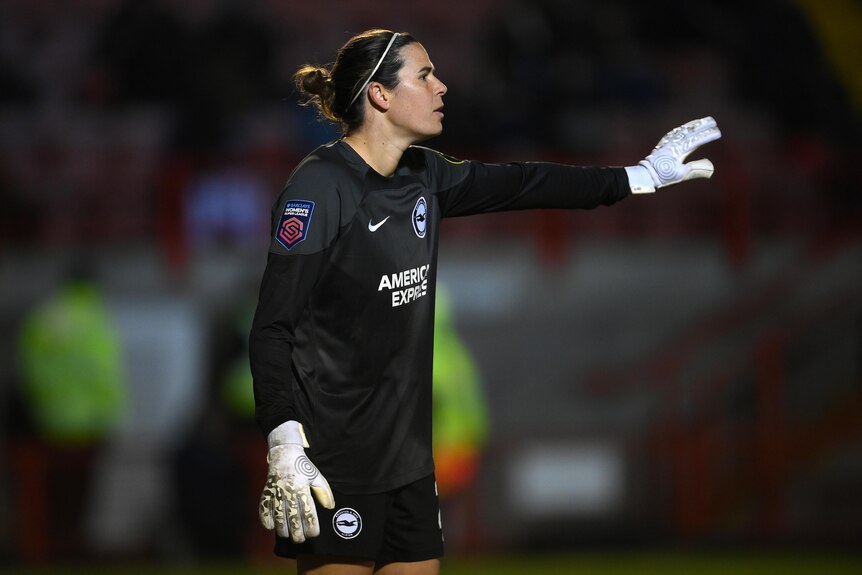 A woman athlete wearing all black and white gloves gestures during a game