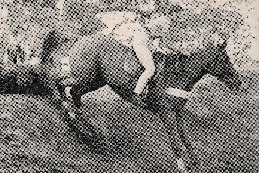 A black and white newspaper image of a rider and horse descending a steep embankment