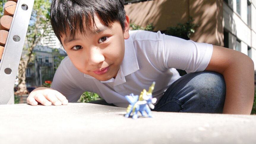 A boy crouched down near a toy figurine