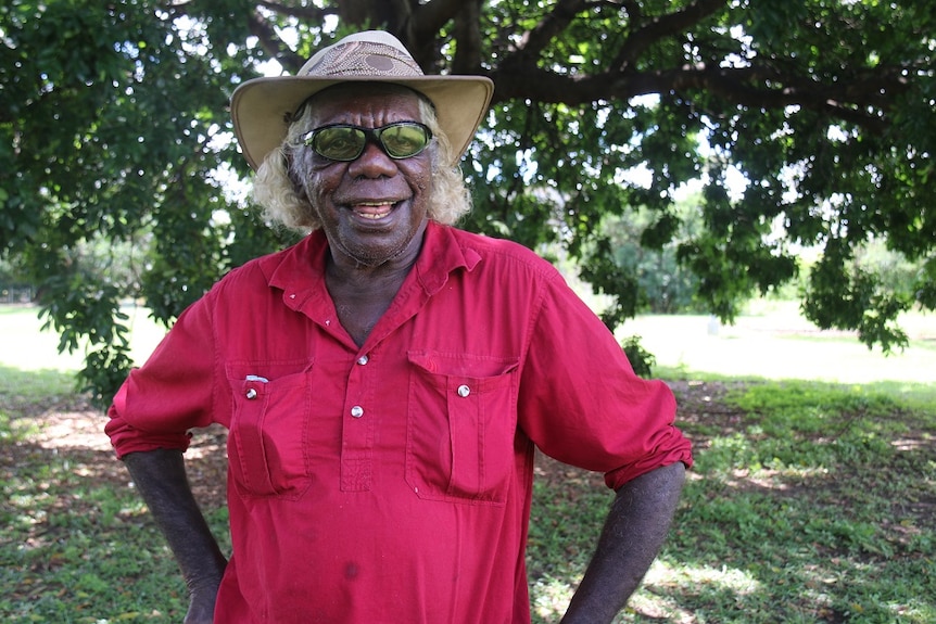 A smiling man wearing a red shirt, a hat and sunglasses.