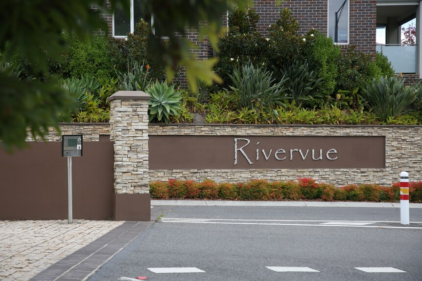 A sign that reads Rivervue on a stone fence, with a garden bed in the background.