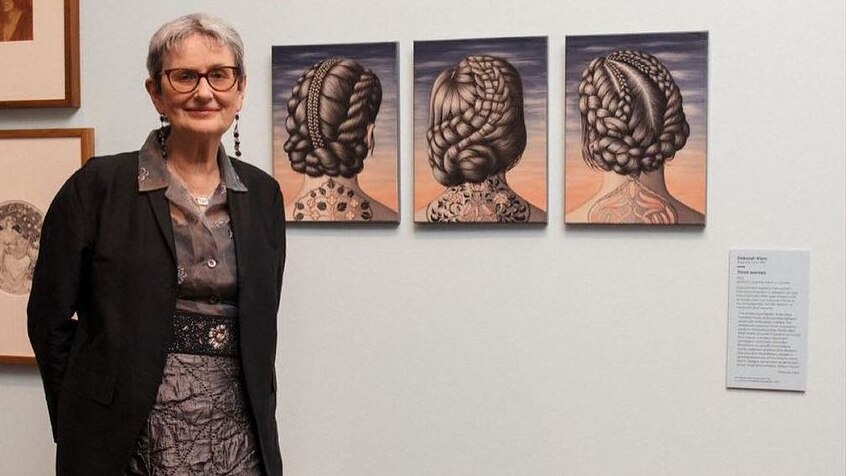 Deborah Klein stands in an art gallery in front of her three works of art called 'three women' 