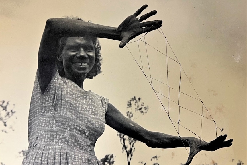 A black and white photograph of a woman holding an Aboriginal string figure with her fingers. 