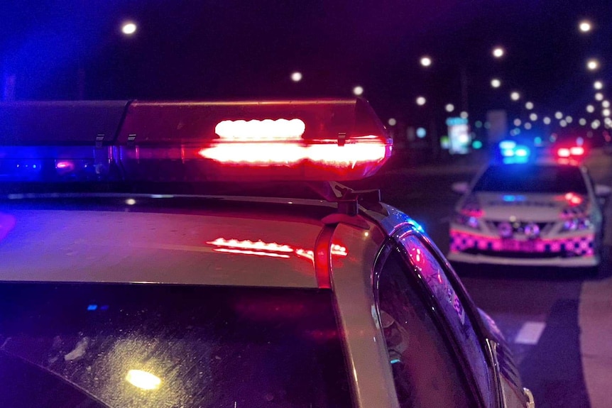 A pair of police cruisers on a road at night with their lights on.